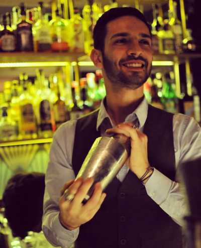 DRINK: GOLDEN MEMORIES (ispirato al film 'Una poltrona per due', di John Landis, 1983)  BARTENDER: Daniele D'Ercole, bar manager di Sacripante Art Gallery di Roma  INGREDIENTI: 6 cl Seven Hills Italian Dry Gin 1,5 cl vermouth dry aromatizzato alla crosta di pane 2 drops di olio evo all'origano e rosmarino   Bicchiere: coppetta cocktail  PREPARAZIONE: Per realizzare il vermouth dry aromatizzato: tostare 20/30 g di croste di pane e lasciarle in macerazione per 3/4 ore in 1l di vermouth dry, filtrare il tutto con un filtro a tessuto. Per realizzare l'olio evo all'origano e rosmarino: riscaldare 100 ml di olio a 60 gradi con un rametto di rosmarino e un cucchiaio di origano, lasciare a fuoco spento per 2 ore e filtrare il tutto. Una volta preparati i due homemade, si realizza il drink, con la tecnica stir & strain. Versare in un mixing glass il Seven Hills Gin e il vermouth dry alla crosta di pane, aggiungere del ghiaccio e miscelare per raffreddare il tutto. Quando ben freddo, filtrare il drink, versarlo nella coppetta precedentemente raffreddata e guarnire con 2/3 gocce di olio aromatizzato, direttamente sopra il cocktail.  ISPIRAZIONE: Un twist del Martini Cocktail, realizzato da Daniele D'Ercole, bar manager di Sacripante Art Gallery, galleria d'arte e cocktail bar in via Panisperna, in pieno quartiere Monti a Roma. Il Martini Cocktail è considerato di per sé un drink signorile e nobile e in questa rivisitazione del classico viene proposto con ingredienti quali pane e olio, alimenti-base e di grande gusto, nonostante, o proprio grazie, la loro umile origine. Un drink che nasce dal ricordo personale del barman, legato alla nonna e alla sua abitudine di preparare una merenda pomeridiana di pane, olio e sale. Profumi e sapori legati a una sensazione di piacere e nostalgia, che ricordano quanto la felicità sia legata all'esperienza delle piccole cose, spesso considerate più scontate, ma che, al contrario, riempiono l'anima. Come nel classico film natalizio, "Una poltrona per due", il drink è la prova che 'l'abito non fa il monaco', sottolineando quanto il valore di una persona si ottenga dalle cose più modeste e dalle esperienze passate. Come il ladruncolo buono, interpretato da Eddie Murphy, diventa broker, qui il pane e l'olio, insieme al fantastico e già perfetto Seven Hills Gin, realizzato con botaniche romane, si trasformano in un drink nobile e da meditazione, per i migliori momenti della nostra vita.