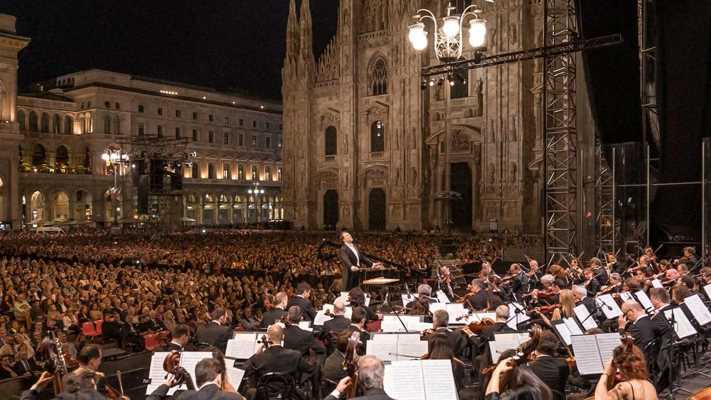Il grande concerto stasera in tv: l'evento di Piazza Duomo che tutti stavano aspettando
Piazza Duomo si trasforma in un grandioso teatro all'aperto. Questo evento speciale unisce migliaia di spettatori sotto il cielo di Milano. Il grande appuntamento annuale della Filarmonica della Scala torna finalmente sul piccolo schermo.
Una volta all'anno la celebre piazza lombarda diventa un vero auditorium. Il pubblico attento crea un silenzio profondo e suggestivo. Riccardo Chailly descrive in questo modo l'atmosfera magica del concerto gratuito. Di conseguenza, l'attesa per l'evento di quest'anno è davvero altissima.
Un evento straordinario nel cuore di Milano
La splendida cornice del Duomo ospita una serata speciale. L'orchestra esce dal tradizionale teatro milanese per incontrare i cittadini. Questo progetto culturale ridisegna il rapporto tra le persone e la grande musica classica. Infatti, la piazza diventa uno spazio di condivisione artistica.
La conduzione della serata televisiva è affidata a Gloria Campaner. La regia dell'evento è invece firmata da Stefania Grimaldi. Sul podio sale il celebre direttore d'orchestra Riccardo Chailly per guidare i musicisti. Per restare aggiornato sugli spettacoli italiani, visita la sezione dedicata su puntozip.net/spettacoli.
Il debutto del pianista dei record
La vera sorpresa di questa edizione è l'ospite solista. Si tratta del giovanissimo pianista giapponese Hayato Sumino. A soli trent'anni, questo straordinario artista vanta numeri da rockstar. Egli unisce un rigore interpretativo impeccabile a una comunicazione molto moderna.
Il musicista è famosissimo sui social network con lo pseudonimo Cateen. Su internet conta infatti oltre due milioni di follower appassionati. Inoltre, ha già conquistato sale prestigiose come la celebre Carnegie Hall. Se ami la grande musica dal vivo, leggi le nostre recensioni su puntozip.net/musica.
Il programma musicale della serata
La selezione dei brani attraversa diverse culture del Novecento. Il repertorio spazia con disinvoltura dall'opera russa al musical americano. Questi mondi sonori creano un unico affascinante viaggio musicale.
Da Rachmaninov all'energia di Gershwin e Bernstein
Il concerto inizia con le vivaci danze dall'opera Aleko di Sergej Rachmaninov. Successivamente, la scena si sposta idealmente oltreoceano con George Gershwin. L'orchestra esegue subito la brillante Cuban Ouverture, scritta dopo un viaggio a L'Avana.
Il vero cuore del programma è il Concerto in fa maggiore per pianoforte di Gershwin. Questo celebre capolavoro unisce la musica classica alle calde sonorità del jazz. Infine, la serata si conclude con le danze sinfoniche di West Side Story di Leonard Bernstein. Pertanto, il ritmo travolgerà l'intera platea milanese.
Come seguire il concerto in televisione
Questo imperdibile evento culturale sarà finalmente accessibile a tutti. Potrai seguire lo spettacolo comodamente da casa tua. Per scoprire altre importanti guide televisive, consulta puntozip.net/televisione.
La trasmissione televisiva va in onda stasera, mercoledì 15 luglio, alle ore 23.50 su Rai 3. Se invece preferisci vederlo in prima serata, l'appuntamento si sposta su Rai 5. Questa seconda visione è prevista per giovedì 16 luglio alle ore 21.20. Sintonizza il tuo televisore per vivere una serata davvero indimenticabile.